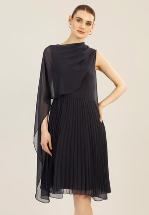 Robe sans manches bleu marine avec jupe plissée, dotée d'un overlay en chiffon asymétrique drapé sur une épaule. Texture lisse, tissu léger.