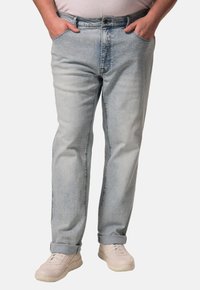 Jeans de mezclilla azul claro con corte recto, cinco bolsillos y puños enrollados. Llevados con zapatillas beige, mostrando un diseño casual.