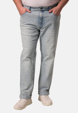 Jeans de mezclilla azul claro con corte recto, cinco bolsillos y puños enrollados. Llevados con zapatillas beige, mostrando un diseño casual.