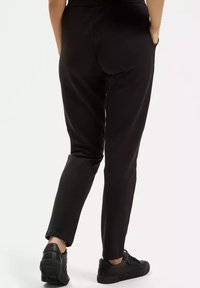 Czarne zwężane spodnie wykonane z gładkiego materiału, z bocznymi kieszeniami i wygodnym pasem, w połączeniu z czarnymi trampkami.