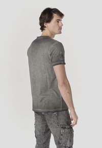 Gray short-sleeve t-shirt with a faded texture, featuring a round neckline and a patch on the left sleeve. Paired with gray cargo pants.