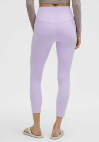 Leggings lilla con una texture liscia e elasticizzata, vita alta e design affusolato. Abbinati a sandali flat.