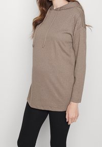 Felpa marrone a coste con maniche lunghe, tasca frontale e cordini regolabili. L'orlo è leggermente più lungo ai lati per garantire maggiore comfort.