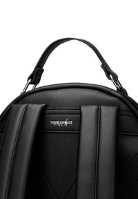 Schwarzer Rucksack aus Kunstleder mit abgerundetem Oberteil, gepolsterten Trägern und subtiler gesteppten Textur. Kleines Logodetail auf der Vorderseite.