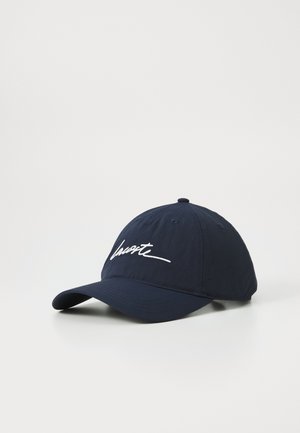 Marineblauwe pet van stof, met een gebogen rand en een witte cursieve logo op de voorkant. Gelaagd oppervlak met stikdetails.