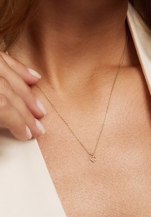 Collier délicat en chaîne d'or avec un petit pendentif cœur ouvert orné d'une seule pierre précieuse claire, porté autour du cou d'une femme.