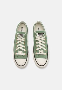 Zielone sneakersy zamszowe z białym gumowym noskiem i podeszwą, złotymi oczkami i kremowymi sznurowadłami. Logo "Converse ALL STAR" na języku.