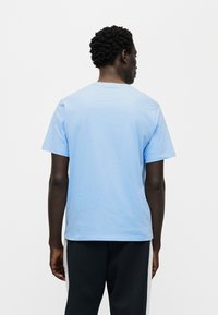 Φωτεινό γαλάζιο βαμβακερό κοντομάνικο μπλουζάκι με στρογγυλή λαιμόκοψη. Εμφανίζεται από πίσω, με λεία υφή και άνετη εφαρμογή.