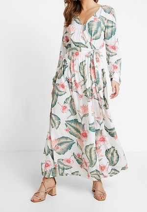 Lange wikkeljurk van een witte stof met groene bladeren en roze bloemmotieven. Heeft lange mouwen en een taille met strikdetail.