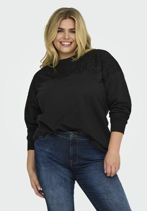 Mustapaita, jossa on pitsiyksityiskohtia olkapäillä, rento istuvuus hihoissa, yhdistettynä tummansinisiin farkkuihin.