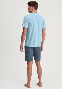 Lichtblauwe katoenen t-shirt gecombineerd met marineblauwe short met patroon. De short heeft een golvend ontwerp en reikt tot halverwege de dij. Schoenen niet zichtbaar.