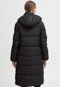 Svart boblejakke med hette, med et quiltet design og ribbede mansjetter. Lang, midt-lår lengde med en glatt, shiny tekstur.