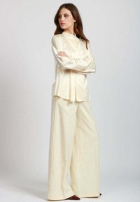 Blusa di seta avorio con collo alto, vestibilità morbida e maniche lunghe, abbinata a pantaloni larghi in tessuto coordinato. Tessuto liscio.