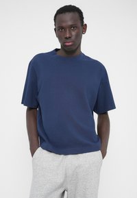 Granatowy T-shirt z krótkim rękawem z miękkiej bawełny o luźnym kroju i okrągłym dekolcie, zestawiony z szarymi spodniami dresowymi ze ściągaczem.