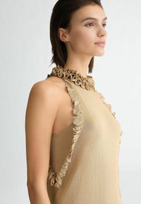Top halter beige con dettaglio arricciato sul collo, realizzato in materiale leggero; presenta una texture liscia e un design aderente.