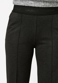 Pantalons de jogging noirs à taille élastique avec un logo de luxe. Dotés d'une texture lisse et de coutures verticales pour un look ajusté.