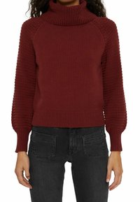 Pull en maille bordeaux avec un col roulé haut, des manches texturées et un ourlet côtelé. Porté sur un jean noir, avec une coupe slim.