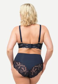 Conjunto de lencería en color navy que incluye un bralette de encaje con tirantes ajustables y un brief de talle alto con acentos de encaje. Textura de tela suave.