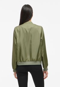Olivovo zelená saténová bomber bunda s ribbed manžetami a lemom. Vyznačuje sa hladkou textúrou a jednoduchým, prispôsobeným dizajnom. Zobrazený pohľad zozadu.