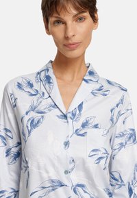 Camicia da pigiama azzurro chiaro con motivo a foglie, colletto a girocollo, dettagli con bottoni e taschino sul petto. Realizzata in tessuto morbido con una texture liscia.