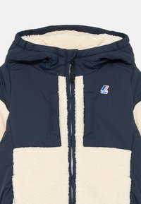 Giacca blu navy con cappuccio, presenta un frontale in pile crema e due tasche sul petto, con un piccolo logo sulla parte sinistra.