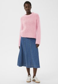Pull rose duveteux avec un col rond, associé à une jupe midi en jean avec des coutures verticales et des baskets blanches à rayures.