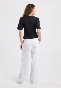 Musta lyhythihainen paita istuvalla siluetilla ja takana rypytetyllä yksityiskohdalla, yhdistettynä löysiin harmaisiin collegehousuihin.