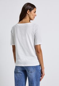 Hvid kortærmet T-shirt med rund hals. Lavet af blødt bomuld, har den en afslappet pasform og en glat overflade. Bagsiden viser et enkelt design.