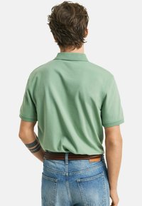 Polo verde a maniche corte realizzato in tessuto leggero, con colletto piatto e vestibilità rilassata, abbinato a jeans in denim blu e una cintura marrone.
