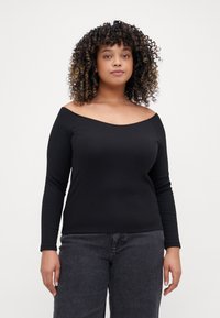 Top negro de manga larga y hombros al descubierto, hecho de tela de canalé, con un diseño ajustado y una textura suave, combinado con jeans oscuros.