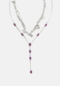 Strieborný viacvrstvový náhrdelník s jedným reťazcom, na ktorom sú fialové obdĺžnikové korálky a visiaca šn�úrka, a druhý reťazec s rôznymi striebornými článkami a priehľadným štvorcovým drahokamom.