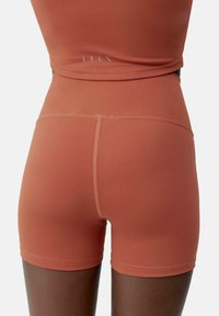 Strakke sportshorts in een roestkleur. Gemaakt van een gladde, elastische stof met zichtbare naaddetails en een hoge tailleband.