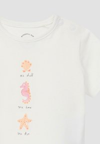 Weißes Babyshirt mit pinkfarbenen Illustrationen von Muscheln, Seepferdchen und Seesternen sowie passenden handschriftlichen Etiketten, mit Druckknöpfen an der Schulter.