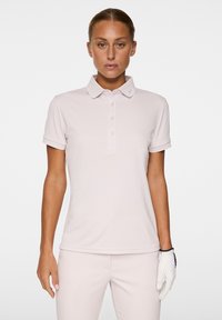 Jasnoróżowa koszulka polo z krótkim rękawem, z plisą zapinaną na guziki i małym logo na kołnierzu; gładka tkanina z dopasowanym fasonem.