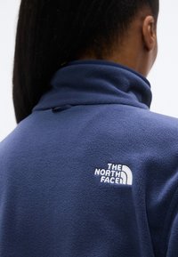 Μπλε σκούρο μπουφάν από μάλλινο fleece με ψηλό γιακά και κεντημένο λευκό λογότυπο στην πλάτη. Μαλακή υφή, σχεδιασμένο για ζεστασιά και άνεση.