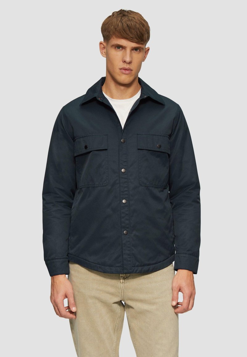 Granatowa kurtka zapinana na guziki, z dwoma kieszeniami na piersi, płaskim kołnierzem i nieco zaokrąglonym dołem. Wykonana z gładkiego materiału.