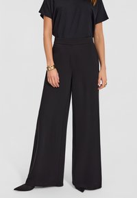 Czarne spodnie o szerokich nogawkach, wykonane z gładkiego materiału, z wysokim stanem, który podkreśla sylwetkę oraz eleganckim krojem.