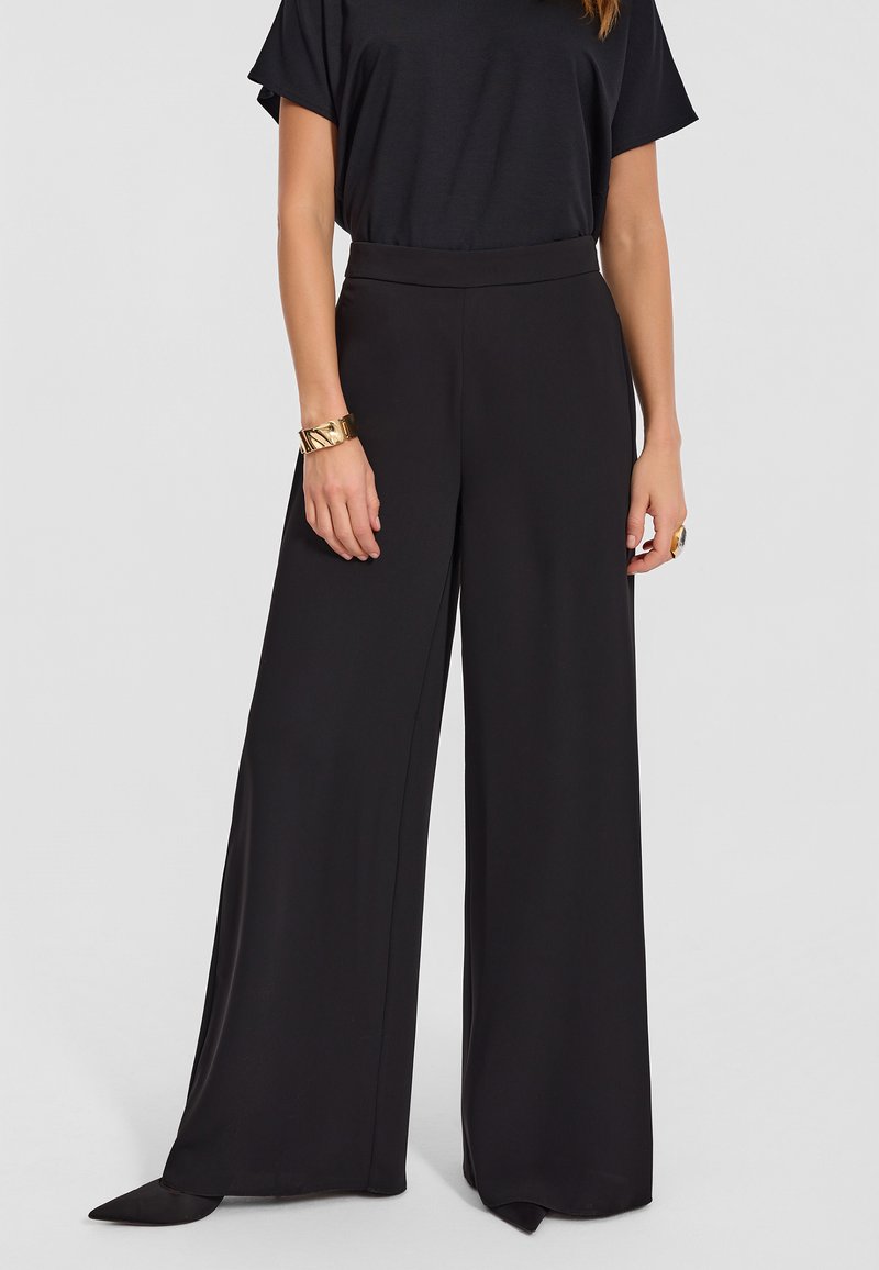 Czarne spodnie o szerokich nogawkach, wykonane z gładkiego materiału, z wysokim stanem, który podkreśla sylwetkę oraz eleganckim krojem.