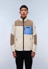 Veste polaire en crème, marron et bleu, avec fermeture éclair frontale, col montant et poche poitrine zippée avec logo de la marque. Tissu texturé.