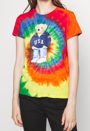 Person trägt ein farbenfrohes Batik-T-Shirt mit einem Bären in einem blauen USA-Sweatshirt und Jeans, die auf der Vorderseite gedruckt sind.