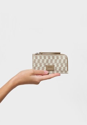 Beige zippered wallet with a repeating abstract pattern, smooth texture, and a metallic logo plate. Held in a hand against a plain background.