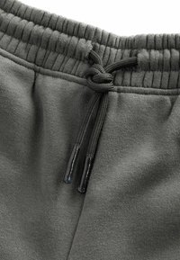 Mørkegrå sweatpants med et tekstureret, blødt stof. Har en elastisk talje med snøre, der afsluttes i blanke sorte spidser.