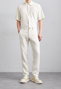 Lyhythihainen, teksturoitu kermavärinen nappipaita yhdistettynä vaaleisiin kermaisiin housuihin ja vaaleisiin liukuvaan kenkiin. Minimalistinen muotoilu, rento malli.