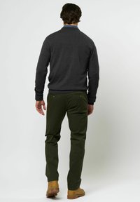 Dunkelgrauer Strickpullover mit gerippten Bündchen, kombiniert mit schmalen olivgrünen Pants und braunen Stiefeln, ausgestattet mit Gesäßtaschen und Knopfdetails.