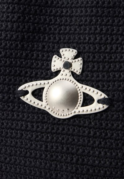 Silver decorative clasp with a round center and bow accent, set against a textured black fabric background. Features small studs along the edges.