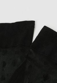 Svart tyg med en strukturerad design som har prickar. De övre kanterna är gjorda av ett glatt material som bildar en krage.