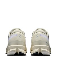 Baskets de course beiges avec une tige texturée, comportant une rayure blanche, un design de talon distinctif et une semelle en caoutchouc à motif.