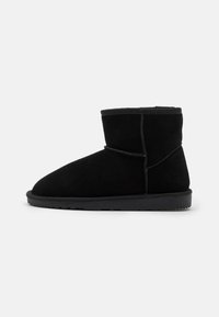 Botines de ante negro con punta redondeada, textura suave y suela de goma flexible. Presentan costuras mínimas y un diseño de altura media.
