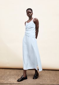 Light blue sleeveless dress with a draped waist and side slit, paired with black slip-on shoes. Smooth fabric texture, minimal design details.