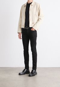 Bežová džínsová bunda, černé tričko s kulatým výstřihem, černé slim-fit džíny a černé šněrovací boty. Bunda má klasický límec a viditelné prošití.